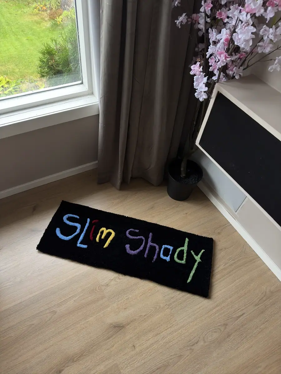 Avlangt svart teppe med håndskrevet tekst i regnbuefarger