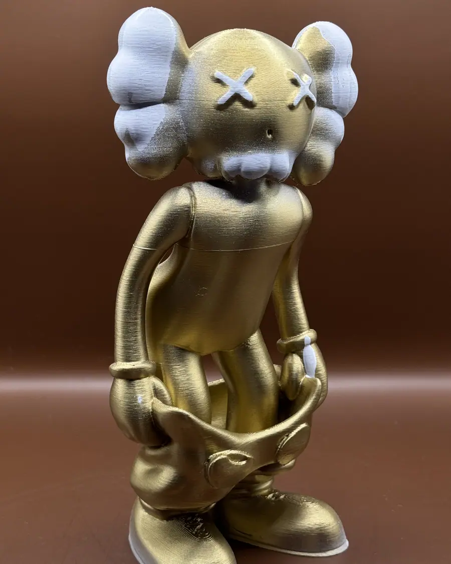 3D-printet figur malt i gull med hvite detaljer, fotografert mot brun bakgrunn